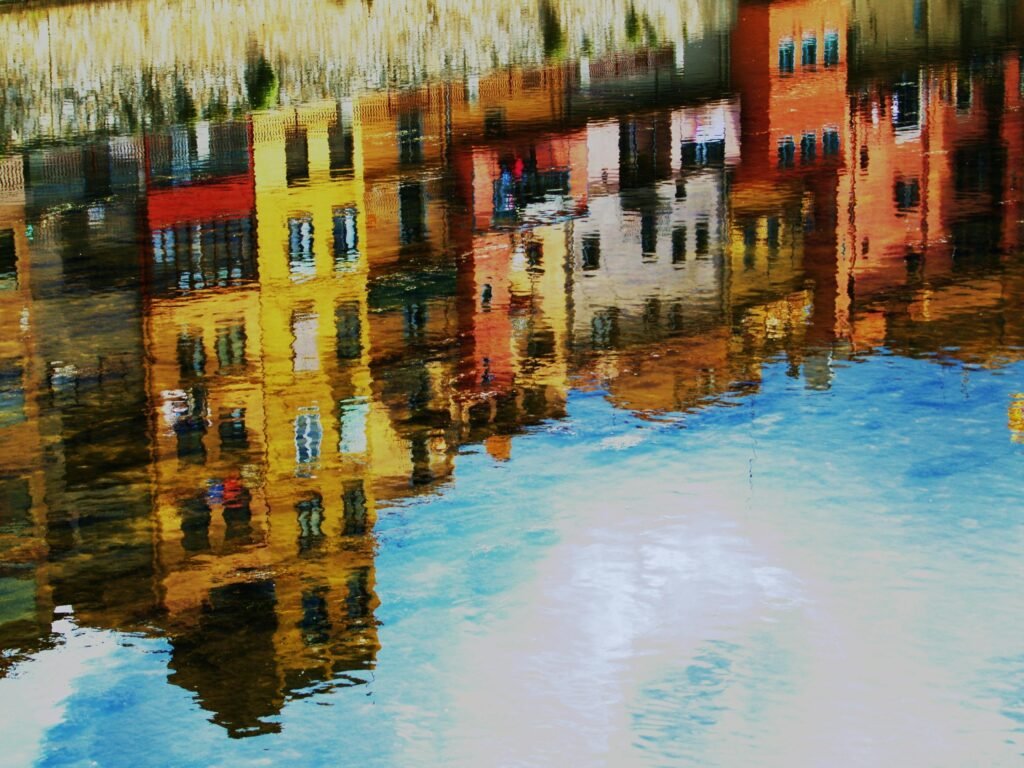 Vibrant reflection of Girona's colorful buildings on a calm river, capturing urban charm.