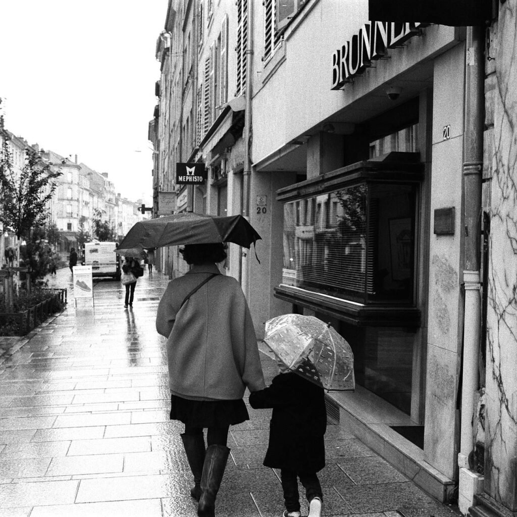 A rainy street in Europe, two people walking with umbrellas.