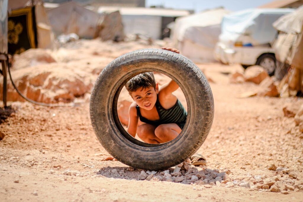 Young boy plays in a refugee camp in Idlib, Syria, using a tire as a toy on a sunny day.