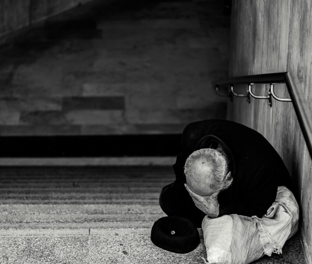 A black and white photo of an elderly man sitting on a staircase, creating a poignant urban scene.