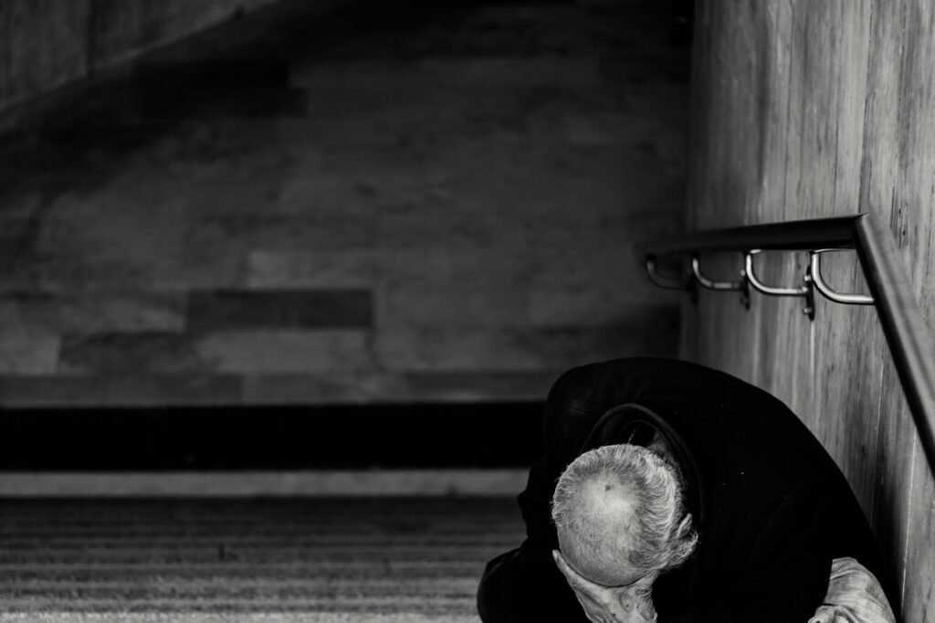 A black and white photo of an elderly man sitting on a staircase, creating a poignant urban scene.